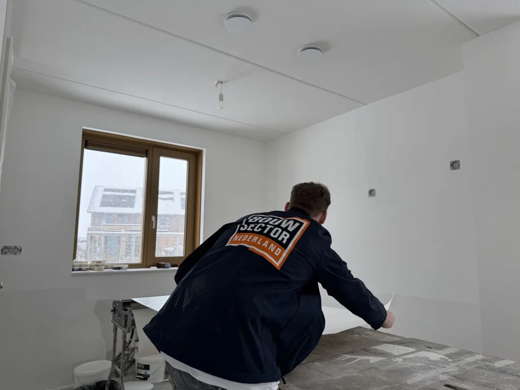 Behanger in werkjas van Bouwsector Nederland pakt een baan van de plaktafel bij het raam