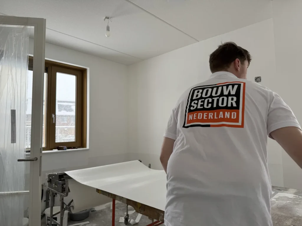Behanger van Bouwsector Nederland bij de plaktafel met een baan wit behang in een nieuwbouwkamer