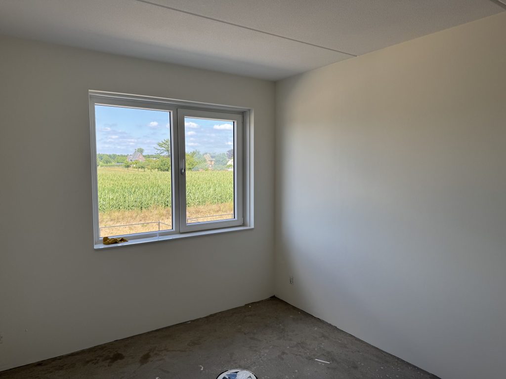Lege slaapkamer in een nieuwbouwwoning met lichte wanden en een raam met uitzicht op een veld