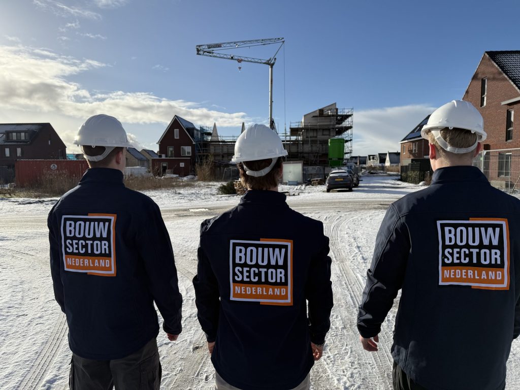 Drie vakmensen van Bouwsector Nederland met witte helm voor een nieuwbouwproject met een bouwkraan